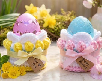 May include: Two decorative Easter egg holders. One has a pink egg and the other a blue egg. Each egg sits in a white, yellow, and pink crocheted holder with a ribbon and a tag that says "For You" and "Happy Easter".
