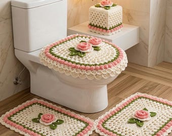 May include: A crochet bathroom set featuring a toilet seat cover, two small rugs, and a tissue box cover. The set is cream-colored with pink and green accents, and each piece is adorned with a pink rose.