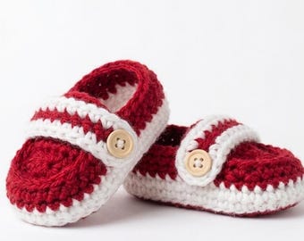 May include: A pair of handmade baby shoes. The shoes are crocheted with a red and white color scheme. The main body of the shoe is red, with a white strap and trim. Each shoe has a wooden button.