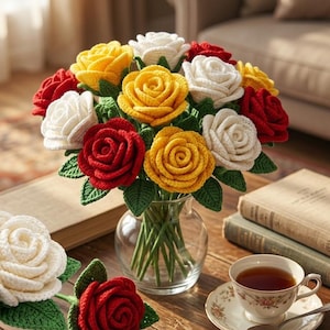 Può includere: Un bouquet di rose all'uncinetto in un vaso di vetro trasparente, con rose singole rosse, gialle e bianche. Una tazza di tè e libri sono su un tavolo di legno, creando un'estetica accogliente e artigianale.