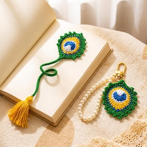 May include: A crochet bookmark featuring a green, yellow, blue, and white peacock feather design with a yellow tassel, alongside a matching keychain with a pearl bead loop and a gold-toned metal clasp, both displaying the same feather motif.