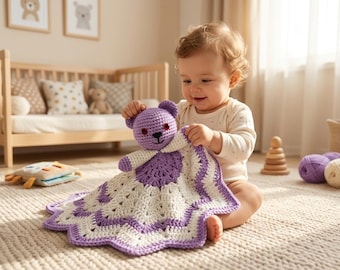 May include: A crocheted baby security blanket featuring a purple teddy bear head and a white and purple patterned blanket. The blanket is held by a baby. The room has a crib, toys, and a rug.
