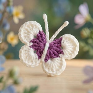 May include: A crocheted butterfly, featuring white wings and a purple body. The butterfly has antennae and is set against a blurred floral backdrop. This handmade item is a decorative craft piece.