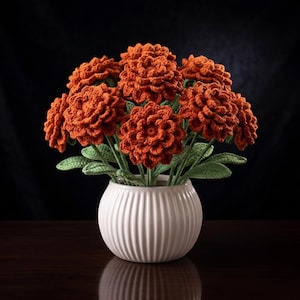 May include: A handcrafted bouquet of orange crochet flowers in a white, ribbed ceramic vase. The flowers have detailed petals and green leaves. The vase sits on a dark wooden surface against a black backdrop, creating a striking contrast.