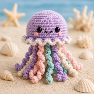 Puede incluir: Un juguete de medusa tejido a ganchillo con cabeza color lavanda, ojos de cuentas negras y mejillas rosadas. Presenta un borde con volantes color crema y múltiples tentáculos en espiral en tonos lavanda, rosa claro, crema y verde menta.