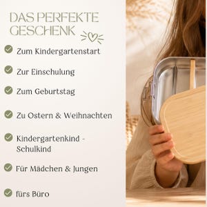 Peut inclure: Une bo&icirc;te &agrave; lunch en acier inoxydable avec un couvercle en bambou est tenue par une personne. Le texte &agrave; gauche indique "DAS PERFEKTE GESCHENK" (Le cadeau parfait) et &eacute;num&egrave;re des occasions telles que "Kindergartenstart" (Rentr&eacute;e scolaire) et "Zum Geburtstag" (Pour l'anniversaire).