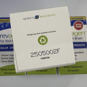 Peut inclure: Bo&icirc;te blanche de compl&eacute;ments alimentaires avec le logo Quincy Bioscience. La bo&icirc;te porte la mention "Package may not be recyclable in your area" et le num&eacute;ro "2505002F". D'autres bo&icirc;tes sont visibles en arri&egrave;re-plan.