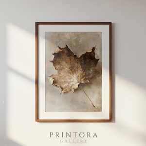 May include: A framed wall art print featuring a single dried brown maple leaf centred on a neutral, textured beige background. The artwork is enclosed in a simple wooden frame. The text PRINTORA GALLERY is visible at the bottom of the image.
