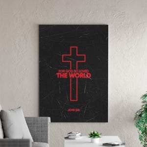May include: A rectangular black canvas print featuring a red cross and the text "FOR GOD SO LOVED THE WORLD" and "JOHN 3:16". The artwork is displayed on a light gray wall above a white table and gray sofa.