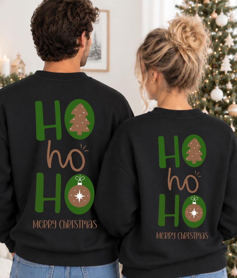Pode incluir: Duas camisolas pretas de gola redonda com uma impress&atilde;o gr&aacute;fica nas costas. O design apresenta o texto HO HO HO em verde e castanho, com uma &aacute;rvore de Natal e um enfeite castanho a substituir as letras O. O texto MERRY CHRISTMAS est&aacute; abaixo.