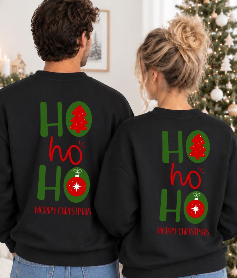 Pode incluir: Duas camisolas pretas de gola redonda com um gr&aacute;fico nas costas apresentando o texto HO ho HO em verde e vermelho. O design inclui uma &aacute;rvore de Natal vermelha dentro de um oval verde e um enfeite de Natal vermelho num oval verde, com Merry Christmas em vermelho.