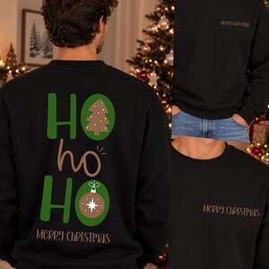 Pode incluir: Uma camisola preta de gola redonda com um gr&aacute;fico nas costas com o texto HO ho HO em verde e castanho, incluindo uma &aacute;rvore de Natal castanha e um ornamento. A zona do peito apresenta o texto MERRY CHRISTMAS em letras castanhas.