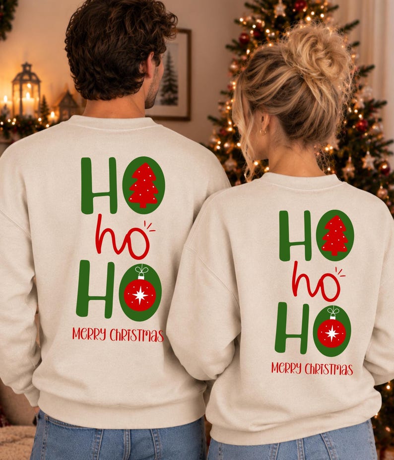 Pode incluir: Duas camisolas bege de gola redonda com um gr&aacute;fico nas costas apresentando o texto verde HO ho HO. O primeiro O cont&eacute;m uma &aacute;rvore de Natal vermelha e o segundo O uma bola de Natal vermelha. O texto vermelho MERRY CHRISTMAS est&aacute; abaixo.