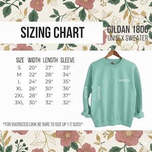 Puede incluir: Una sudadera unisex Gildan 1800 de color verde azulado claro cuelga de una percha de madera. La imagen incluye una tabla de tallas con medidas en cent&iacute;metros para el ancho, el largo y el largo de la manga, que van desde la talla S hasta la 3XL. El texto dice "TABLA DE TALLAS".