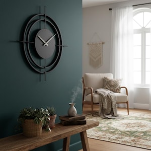 Può includere: Un orologio da parete moderno in metallo nero con un quadrante ovale grigio e lancette argentate. L'orologio presenta un design unico con due cerchi concentrici e barre verticali e orizzontali. È montato su una parete verde scuro.