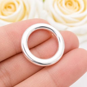 Peut inclure: Un anneau circulaire en argent poli avec une surface lisse et arrondie. La bande métallique présente une finition réfléchissante très brillante et une épaisseur constante sur toute sa circonférence, offrant une forme géométrique simple.