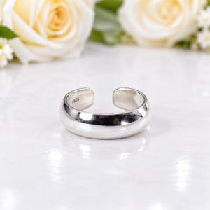 Peut inclure: Une bague ouverte en argent poli avec une surface lisse et arrondie. L'intérieur de l'anneau porte clairement le poinçon 925, indiquant une composition en argent sterling. La bague présente un design simple et continu avec une ouverture.