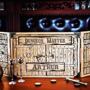 May include: A wooden Dungeon Master screen with the text "Dungeon Master" and "Arthur" engraved on it. The screen has a rustic design with metal corner reinforcements. A brass pitcher, two goblets, and other game accessories are in front.