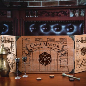 May include: A three-panel wooden game master screen featuring laser-engraved stone wall patterns, banners, and a central gate design with a 20-sided die icon and the text GAME MASTER. A brass-coloured metal pitcher and two small metal goblets sit nearby.