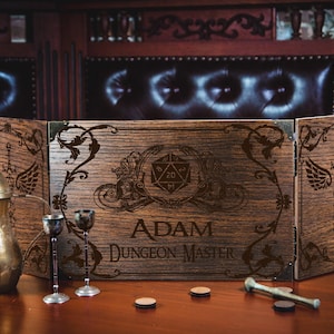 May include: A wooden tabletop gaming screen with engraved designs and the text "ADAM DUNGEON MASTER." The screen is flanked by a brass coffee pot, two small goblets, and game tokens. The background features a dark, ornate wooden interior.