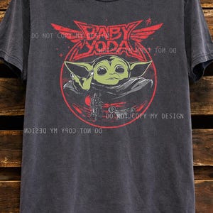 Oversized faded black graphic t shirt featuring a retro inspired baby alien character design with red and green vintage sci fi artwork, unisex casual streetwear tee for space fantasy fans.