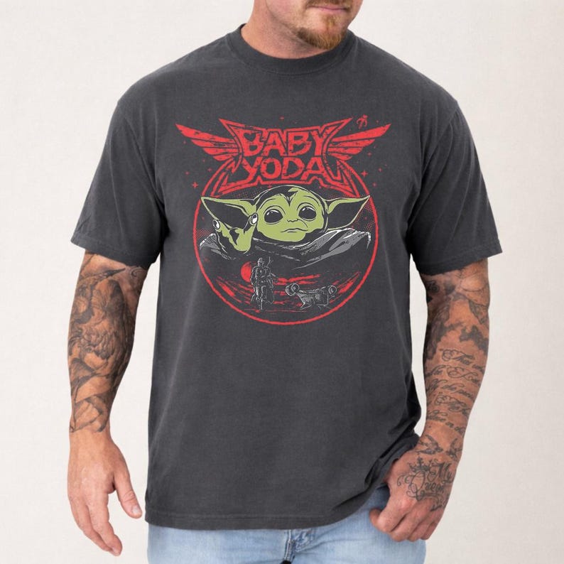 May include: Dark gray t-shirt featuring a graphic of Baby Yoda with the text "Baby Yoda" in red. The design includes a red circle and wings. The shirt is short-sleeved and has a crew neck.