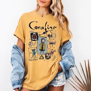 May include: A mustard yellow short-sleeve t-shirt featuring a black graphic print with the text Coraline. The design includes a central illustration of a character in a yellow coat surrounded by smaller drawings of a cat, a key, and creatures.