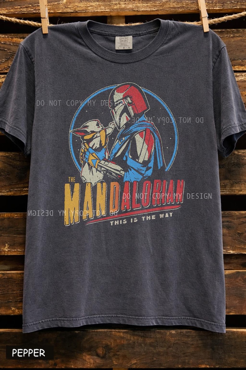 Pu&ograve; includere: T-shirt grigio scuro con una grafica vintage di The Mandalorian e Grogu. Il design include il testo "THE MANDALORIAN" e "THIS IS THE WAY". La maglietta &egrave; realizzata in un materiale morbido.