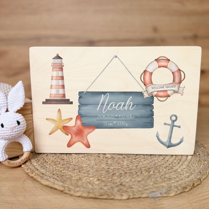 A light wooden box with a nautical design on its lid, featuring a lighthouse, starfish, a lifebuoy with "WELCOME ABOARD" text, an anchor, and a hanging sign with "Noah" and birth details.
