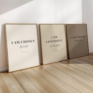 Pode incluir: Três impressões de arte emolduradas com citações inspiradoras. As impressões têm um fundo bege com molduras douradas. As citações dizem: "I AM CHOSEN by God", "I AM CONFIDENT in His plan" e "I AM STRONG through Him". As impressões estão encostadas em uma parede branca em um piso de madeira.