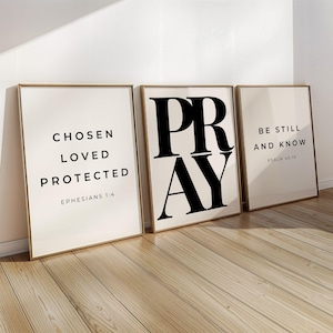 Puede incluir: Tres impresiones artísticas enmarcadas con citas inspiradoras. La primera impresión dice "CHOSEN LOVED PROTECTED" con "EPHESIANS 1:4" debajo. La segunda impresión dice "PRAY". La tercera impresión dice "BE STILL AND KNOW" con "PSALM 46:10" debajo.