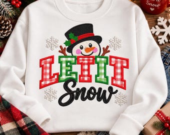 Könnte beinhalten: Ein weißes Langarm-Sweatshirt mit einem gestickten Schneemann, der einen schwarzen Zylinder mit Stechpalmen trägt. Der Text LET IT SNOW ist in rot-grün karierten Blockbuchstaben und schwarzer Schreibschrift dargestellt, umgeben von Schneeflocken.