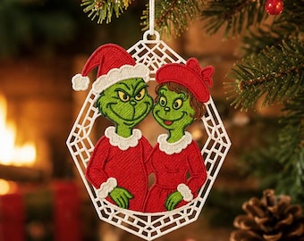 Könnte beinhalten: Ein weißes, geometrisches, lasergeschnittenes Ornament mit einer Stickerei von zwei grünen Figuren. Eine trägt eine rote Weihnachtsmütze und einen roten Mantel mit weißem Besatz, die andere einen roten Hut und ein rotes Kleid mit weißem Besatz.