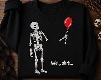 Könnte beinhalten: Ein schwarzes Sweatshirt mit Rundhalsausschnitt und einer weißen Stickerei eines Skeletts, das mit abgetrenntem Arm einen roten Luftballon an einer Schnur hält. Der Text "Well, shit..." ist in Weiß unter dem Skelett auf der Vorderseite gestickt.