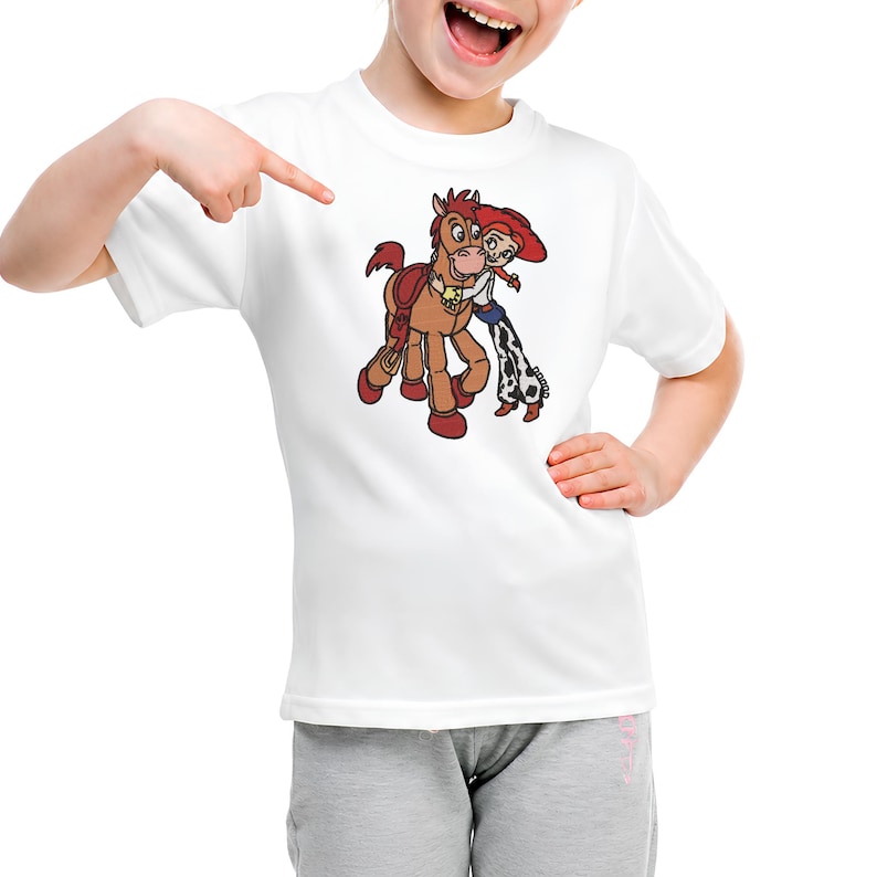 Puede incluir: Una camiseta blanca de manga corta con un estampado gr&aacute;fico de un caballo marr&oacute;n con una silla de montar roja y una vaquera de pelo rojo, sombrero rojo y pantalones con manchas de vaca abrazando el cuello del caballo con cari&ntilde;o.