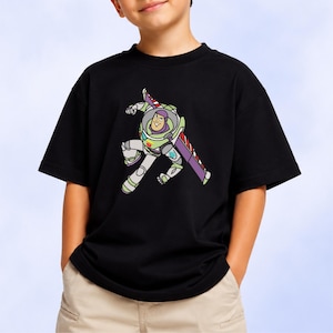 Puede incluir: Una camiseta negra de manga corta con un estampado gr&aacute;fico de un personaje de ranger espacial con un traje blanco, verde y morado con alas extendidas. El personaje aparece en una pose din&aacute;mica con una expresi&oacute;n sonriente en el pecho.