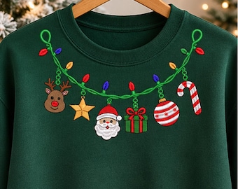 Könnte beinhalten: Ein dunkelgrüner Rundhals-Pullover mit einer Stickerei, die eine grüne Lichterkette zeigt, welche über die Brust drapiert ist. Die Lichterkette ist mit hängenden Ornamenten wie einem Rentier, einem Stern, dem Weihnachtsmann, einem Geschenk und einer Zuckerstange verziert.