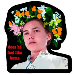 May include: A sticker featuring a portrait of a person wearing a floral crown, with the text "does he feel like home" in red. The person is wearing a white shirt with blue accents and a black border.