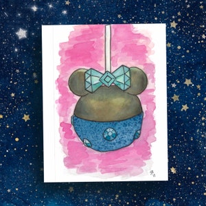 May include: Watercolor illustration of a candy apple with a bow and blue accents. The candy apple is brown with a blue bow and blue accents. The background is pink and the paper is white.