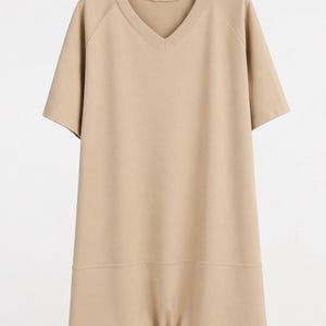 Pode incluir: Um vestido t-shirt bege liso com decote em V, mangas curtas e um detalhe de costura horizontal na parte inferior. A peça apresenta um corte relaxado, um decote simples e uma bainha reta, apresentada num cabide de plástico preto.
