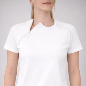 Op de afbeelding: Wit T-shirt met korte mouwen en een uniek ontwerp. Het shirt heeft een witte rits die van de schouder naar de kraag loopt. De rits is wit en past bij de kleur van het shirt. Het shirt heeft een ronde hals en een eenvoudige, moderne stijl.