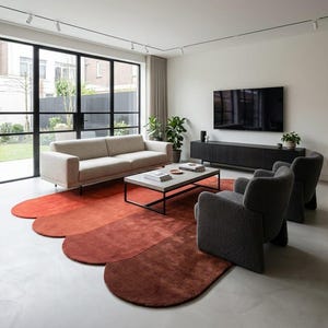 May include: A modern living room featuring a beige sofa, two gray armchairs, and a coffee table on a unique, multi-toned red rug. A large TV is mounted on a dark wood cabinet. Large windows offer a view of the outdoors.