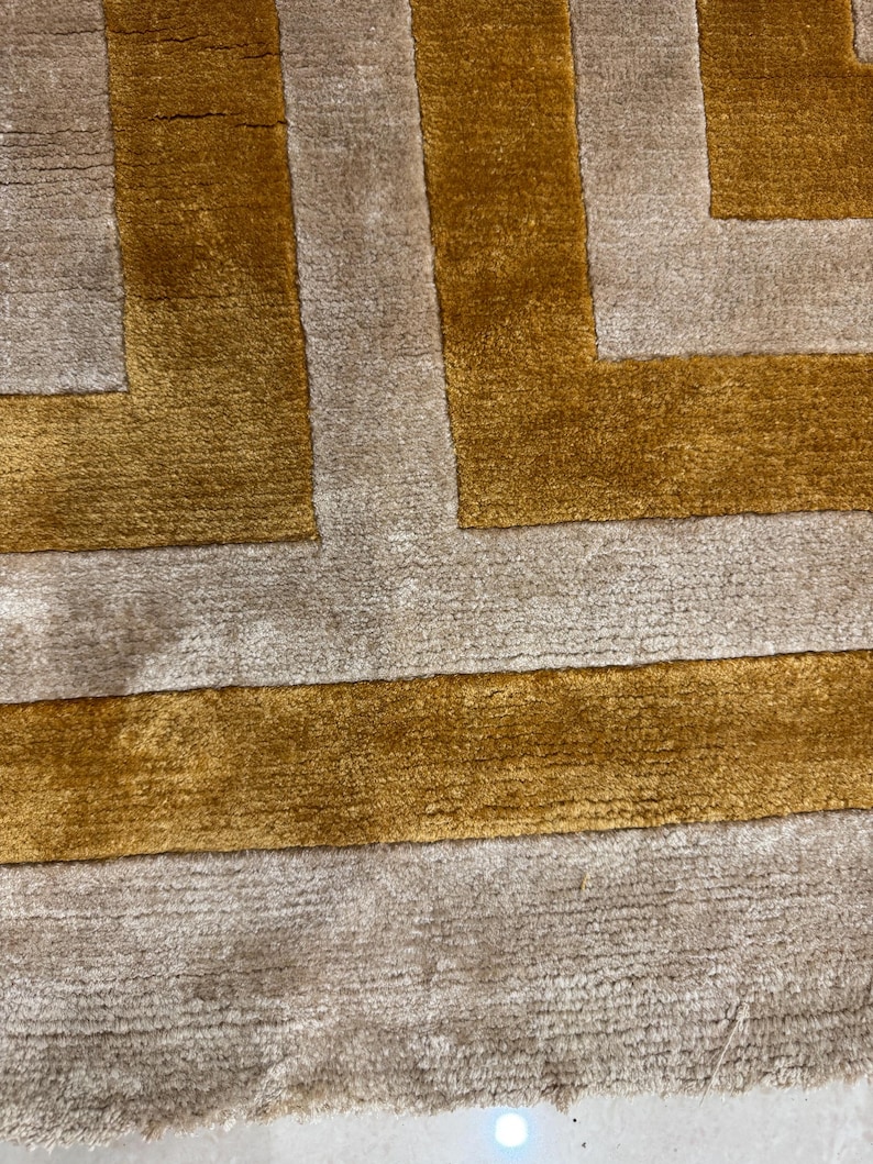 Puede incluir: Una alfombra rectangular con un patr&oacute;n geom&eacute;trico de bandas alternas en color amarillo mostaza y beige claro. La alfombra presenta una textura densa de pelo corto con l&iacute;neas horizontales visibles y un aspecto suave y afelpado.