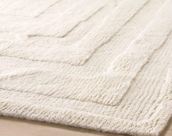 Puede incluir: Alfombra texturizada de color crema con un patrón geométrico. La alfombra presenta una serie de formas rectangulares en relieve dispuestas en un diseño en zigzag. La textura afelpada y el color neutro de la alfombra la hacen adecuada para varios estilos de interior.