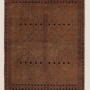 May include: A rectangular brown area rug featuring a dark brown geometric pattern of interconnected diamonds, vertical lines, and small dots. The rug is framed by a border of repeating triangular shapes and includes white fringe at both ends.