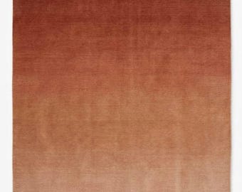 Puede incluir: Una alfombra rectangular con un degradado de color. La alfombra pasa de un marrón rojizo oscuro en la parte superior a un marrón claro, beige en la parte inferior. La textura parece suave y afelpada, adecuada para un espacio habitable.