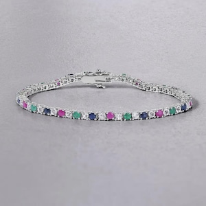 Könnte beinhalten: Ein silberfarbenes Tennisarmband mit einem sich wiederholenden Muster aus runden, klaren, blauen, grünen und rosafarbenen Edelsteinen, die in eine durchgehende Metallkette gefasst sind. Das Armband verfügt über einen sicheren Kastenschloss-Verschluss.