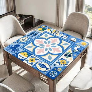 May include: A square wooden table with a blue, white, and yellow patterned top. The design features floral and nautical motifs, including fish, an octopus, and a sailboat. The table is surrounded by light-colored chairs.
