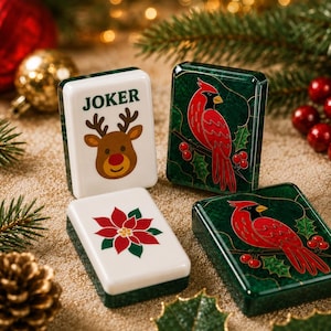 May include: Four rectangular mahjong tiles with festive designs. One white tile features a brown reindeer and the text JOKER. Another white tile displays a red poinsettia. Two dark green tiles feature a red cardinal bird perched on a branch.