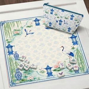 May include: A square fabric mat and a matching zippered pouch featuring a blue and white print of cranes, lotus flowers, willow trees, and pagodas. Several white rectangular mahjong tiles with colourful floral and bird motifs are scattered on the mat.